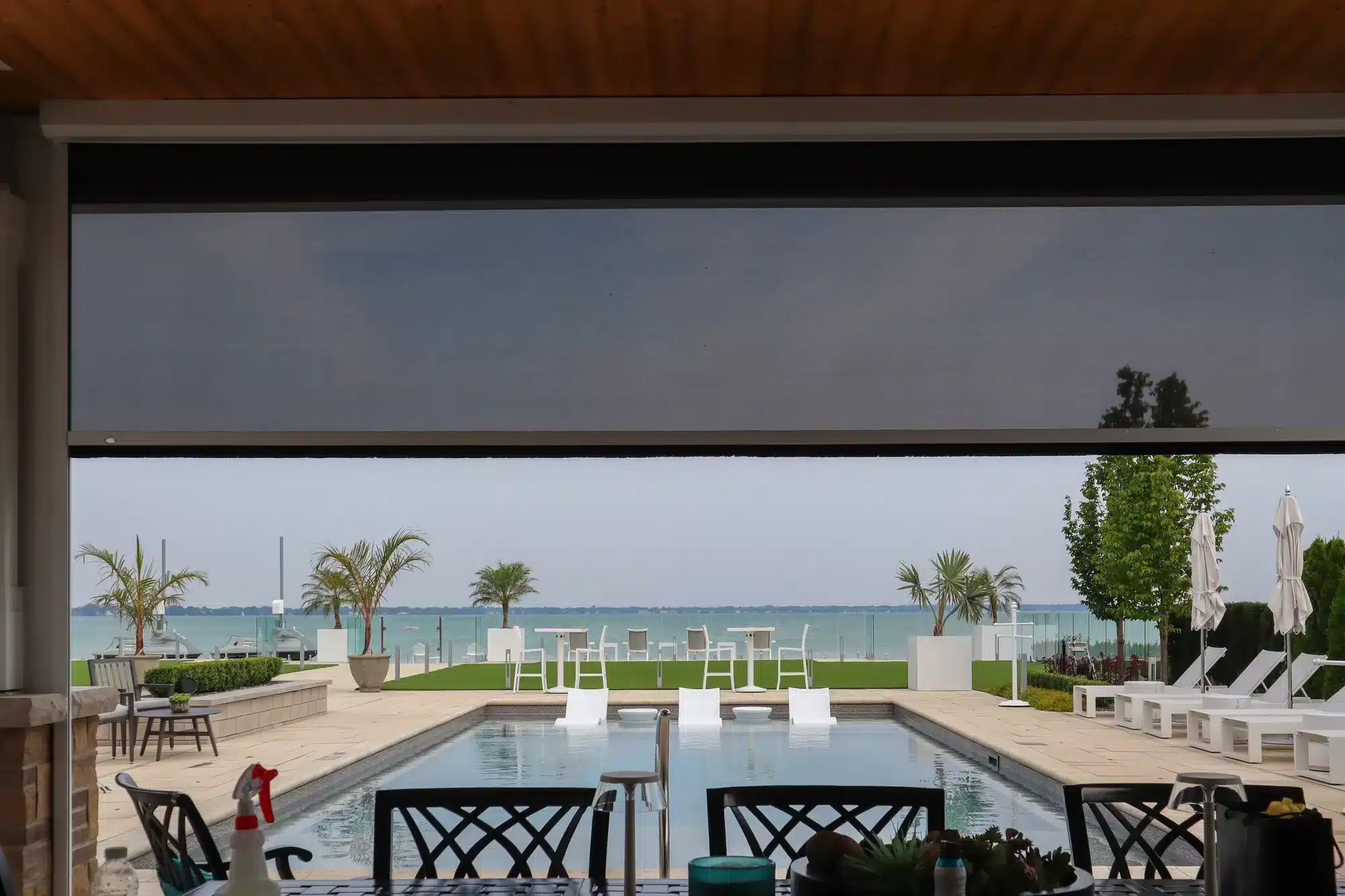 View of a swimming pool and lake through a black retractable weather screen.