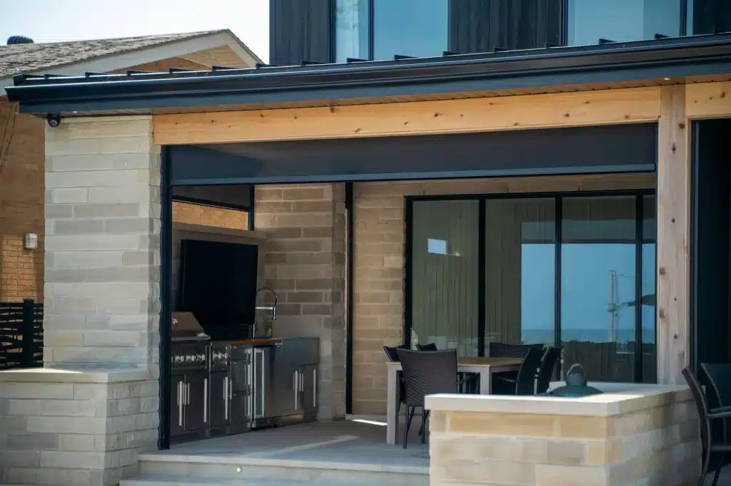 Covered outdoor kitchen with black retractable privacy screens and dining area.