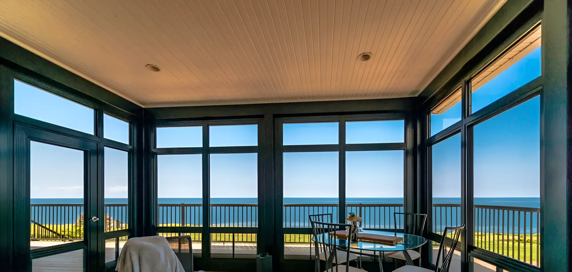 Interior of a sunroom with black frames, large windows, and a dining set overlooking the ocean.