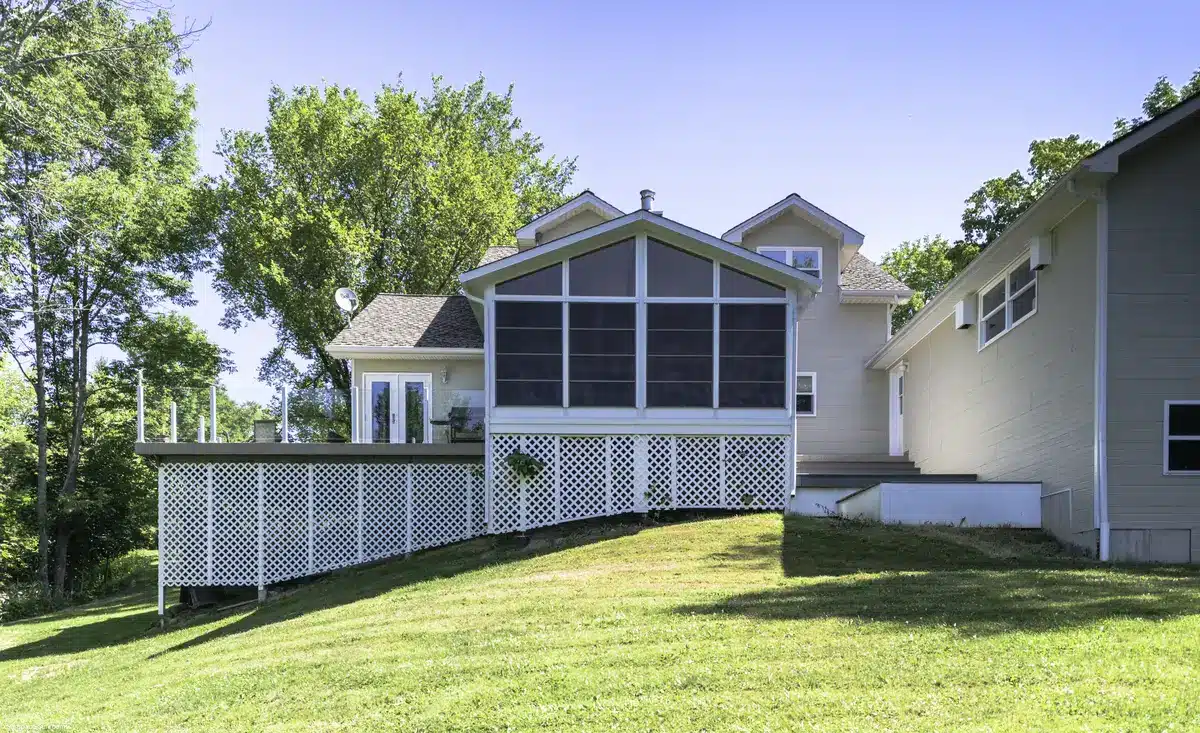 Exterior view of a house with a Sunspace sunroom enclosure and an adjacent deck with white railing.